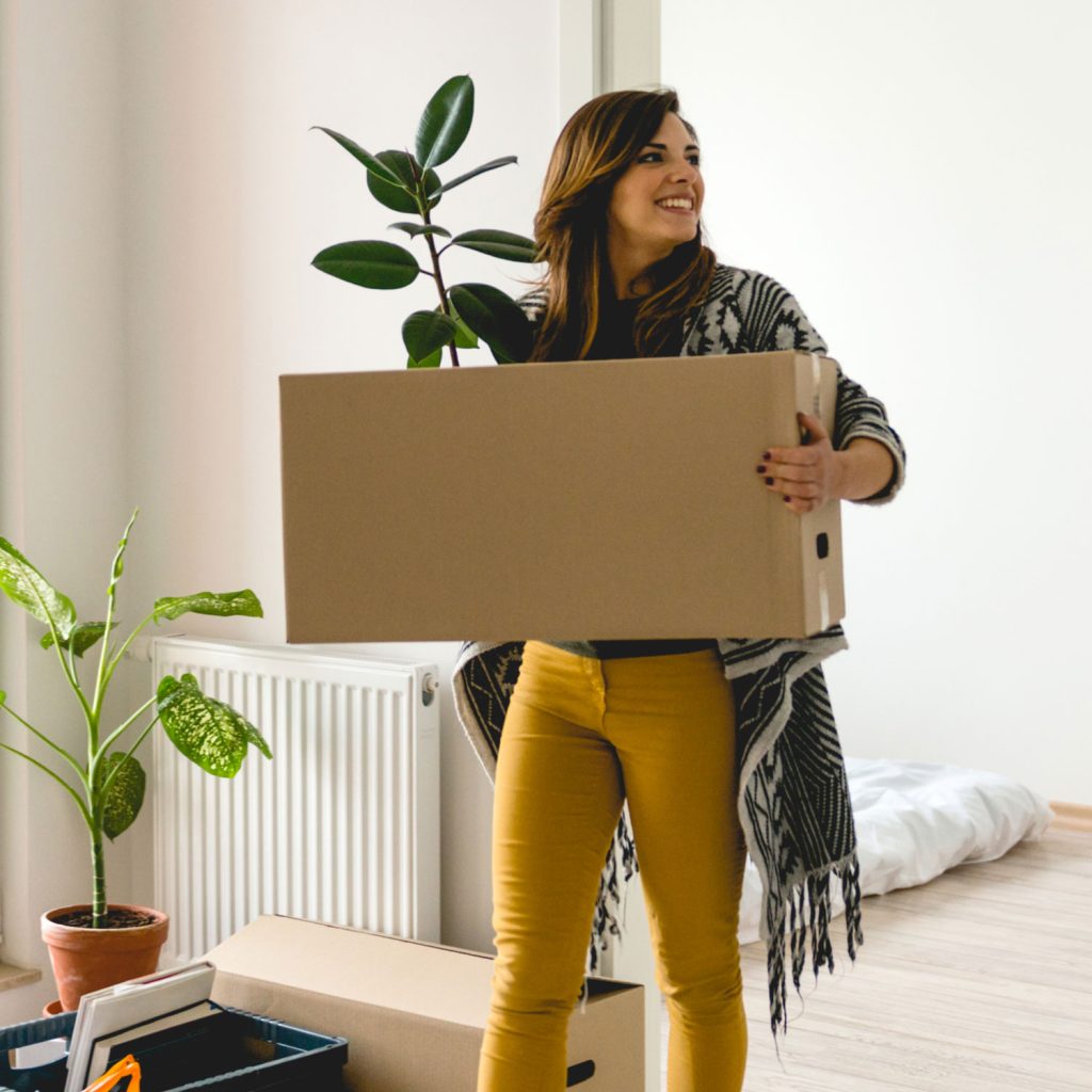 Smiling young woman carrying moving boxes through her new home