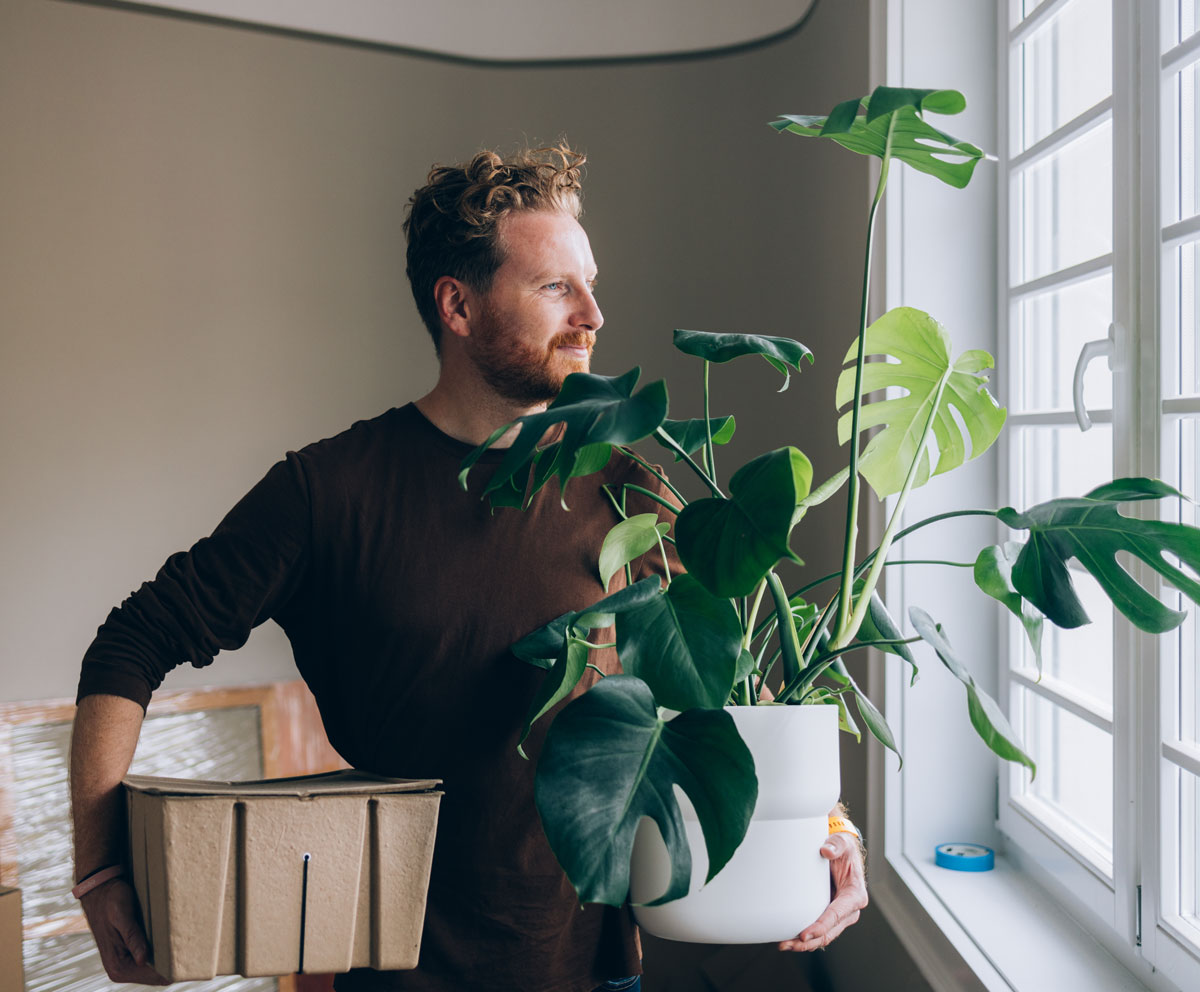 Photo of a smiling first home buyer carrying a pot plant as he moves into his first home